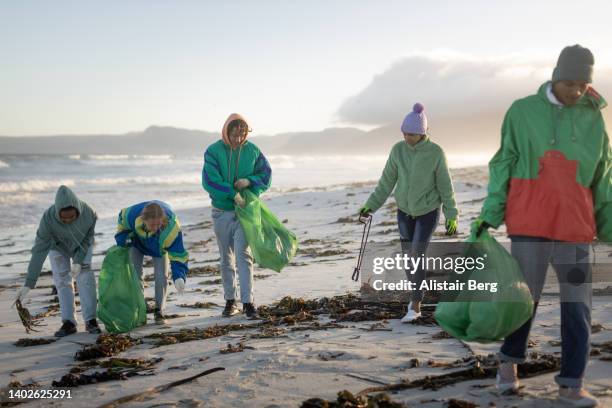 group of young people cleaning rubbish from a beach - organisation environnement stock-fotos und bilder