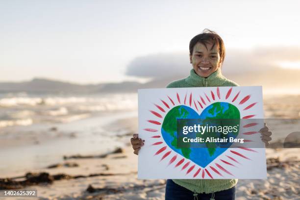 young woman holding up an eco awareness placard on a windswept beach - person holding up sign stock-fotos und bilder