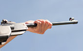 A hand holds the barrel of an air rifle against a blue sky