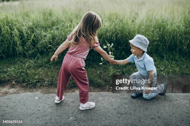 a little boy gives a bouquet of wildflowers to a little girl. - man giving flowers stock-fotos und bilder