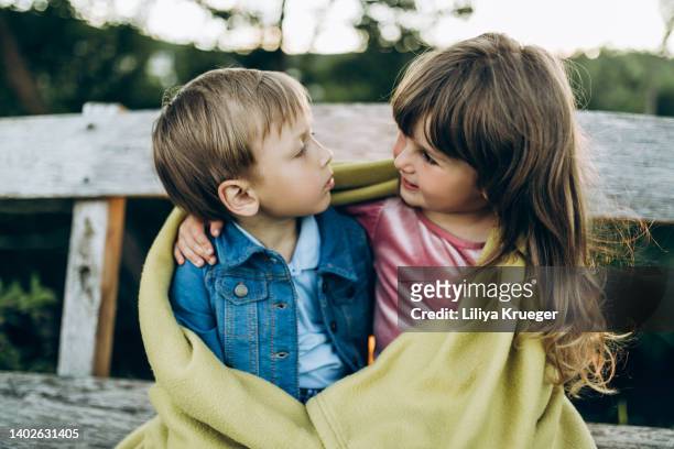 beautiful little boy and girl are warming themselves under one blanket. - siblings stock-fotos und bilder