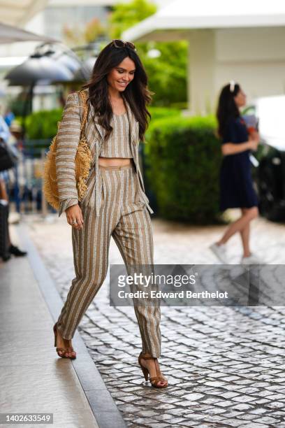 Diane Leyre wears brown sunglasses, a brown beige and white striped print pattern linen V-neck / cropped t-shirt, a matching brown beige and white...