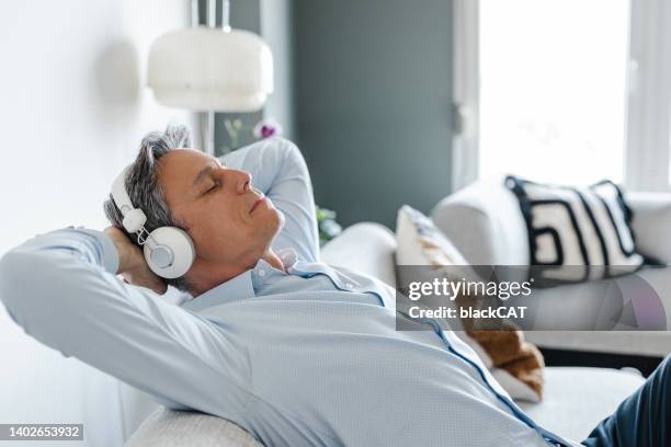 mature man relaxing at home and listening to music - white sofa stock pictures, royalty-free photos & images