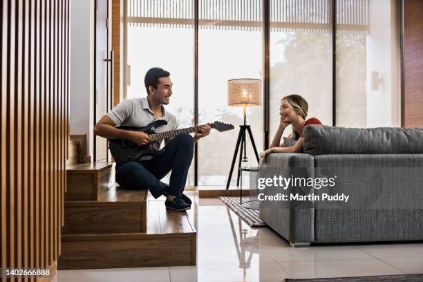 young multiracial couple relaxing at home, playing guitar while sitting in modern living room - fabolous musician stockfoto's en -beelden