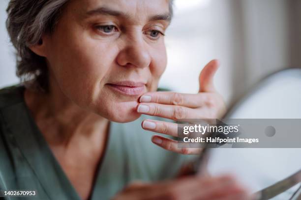 mature woman taking care of skin at home. close-up. - adult in mirror stock-fotos und bilder