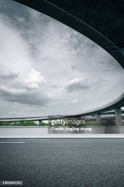 asphalt road crossing under viaduct under cloudy sky - pech stock-fotos und bilder