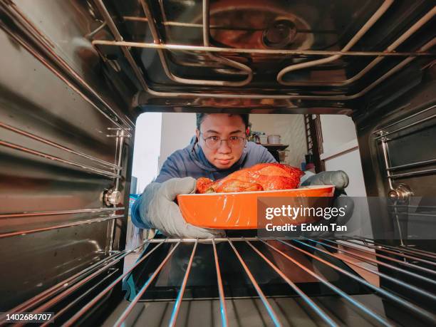 asain chinese mid adult man retrieving roast chicken from electronic oven with protective glove  learning new skill cooking cooking roast chicken at home - new home pov stock pictures, royalty-free photos & images