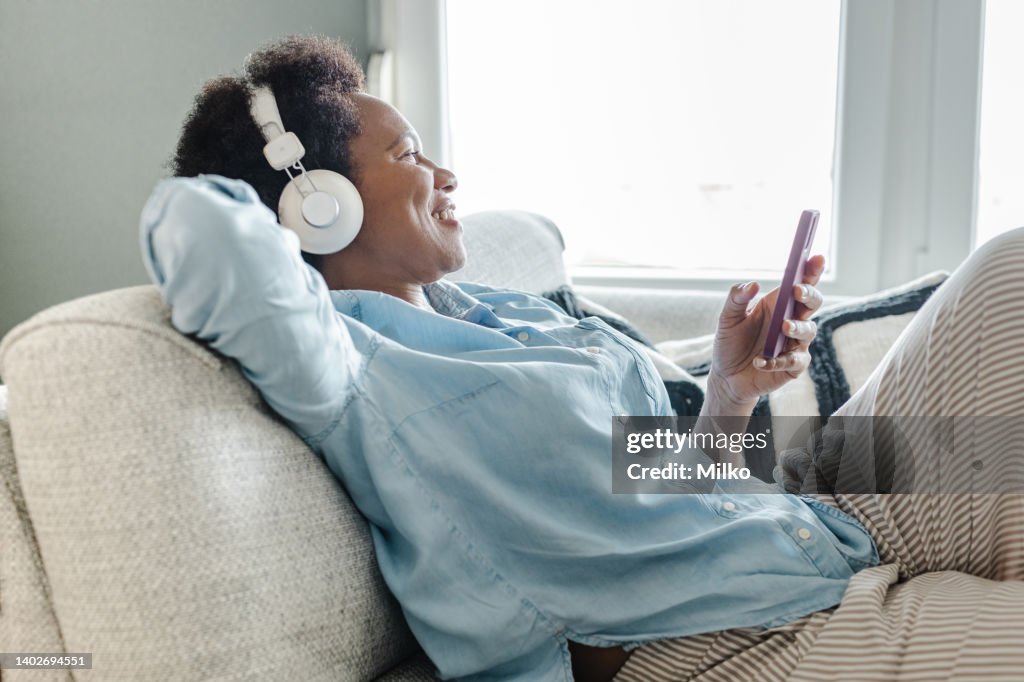 Mujer afroamericana relajándose en el sofá usando un teléfono inteligente