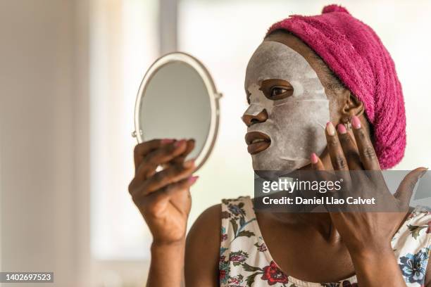 woman applying facial mask while looking a mirror. - mascarilla stockfoto's en -beelden