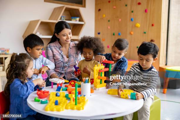 teacher with a group of elementary students playing with toy blocks - cuidar de crianças imagens e fotografias de stock
