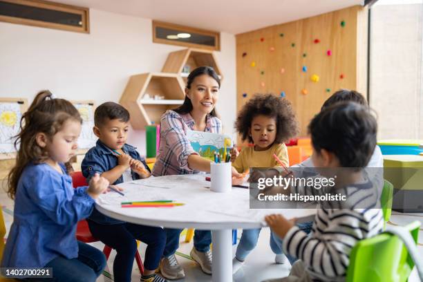 grupo de niños coloreando en clase de arte con la supervisión de su profesor - maestro fotografías e imágenes de stock