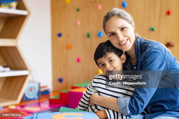 happy teacher hugging a young student at the school - teacher pre school imagens e fotografias de stock