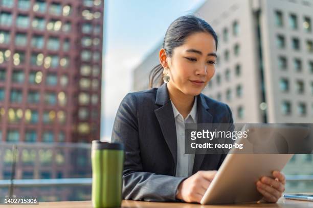 young business woman in full suit using digital tablet in financial district in city - east asian ethnicity stock pictures, royalty-free photos & images
