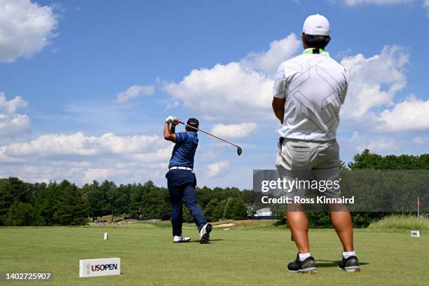 Hideki Matsuyama of Japan plays his shot from the eighth tee as caddie Shota Hayafuji looks on during a practice round prior to the 2022 U.S. Open at...