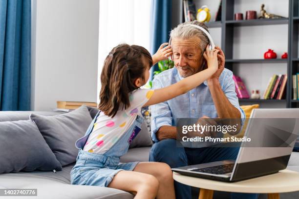 grandchild is making his grandfather listen to music on the computer and they are having fun - old arab man stock pictures, royalty-free photos & images