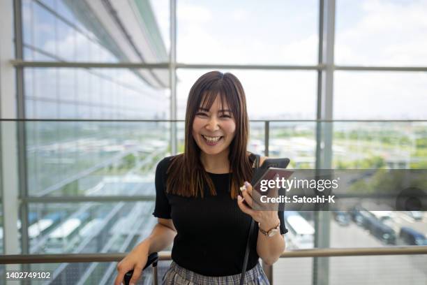 空港で幸せな女性の肖像画、スマートフォンとパスポートを持っている - 日本人　空港 ストックフォトと画像