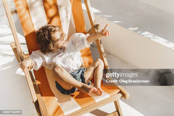 sweet cute baby enjoying on sun bed or chaise lounge. summer children fashion style - baby sun hat stock-fotos und bilder