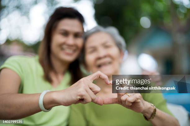 shot of smiling senior mother and daughter making a heart shape with their hands. - nur erwachsene stock-fotos und bilder
