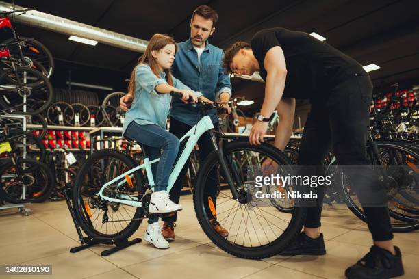 salesman showing father and daughter new bicycles in bike shop - single father stockfoto's en -beelden