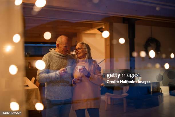 seniors standing at window, during winter evening. trough window view. - fireplace cosy stock pictures, royalty-free photos & images