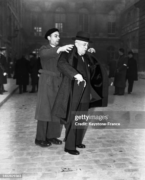 Homme politique Henri Queuille se fait aider de son chauffeur pour remettre son pardessus le 17 décembre 1953.