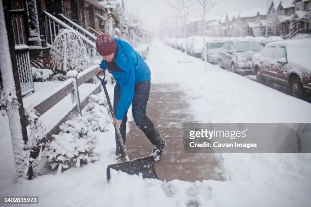 a man shovels the sidewalk outside of his suburban house. - snow shovel man stock pictures, royalty-free photos & images