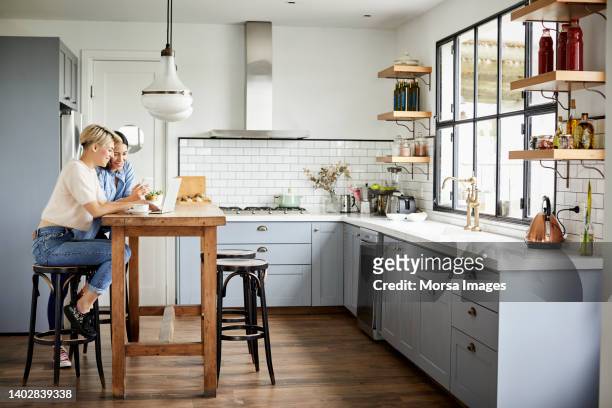 smiling friends using laptop in kitchen - man proposing indoor stock-fotos und bilder