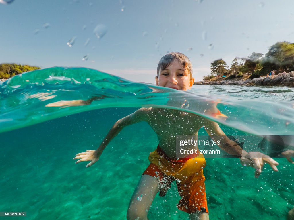 Ragazzo felice in costume da bagno che gioca in mare, scattato con una fotocamera impermeabile indossabile