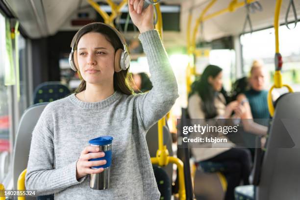 woman whit headphones standing in a bus and holding coffee - public transportation stockfoto's en -beelden