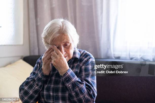 portrait of a sad senior woman wiping her tears at home. - teardrop stock pictures, royalty-free photos & images