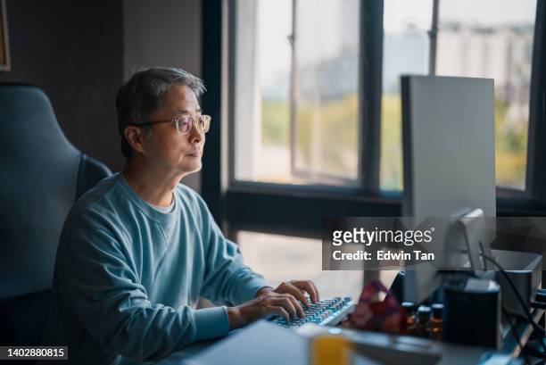 asiatisch-chinesischer reifer mann arbeitet von zu hause aus, tippt und schaut in seinem heimbüro auf den computer - mann vor pc stock-fotos und bilder