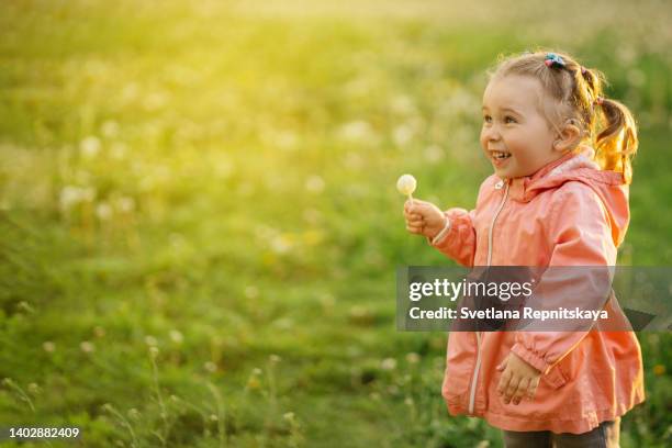 smiling baby girl with cochlear implants walks on a green lawn with a lollipop in hand outdoors at sunset - one baby girl only fotografías e imágenes de stock