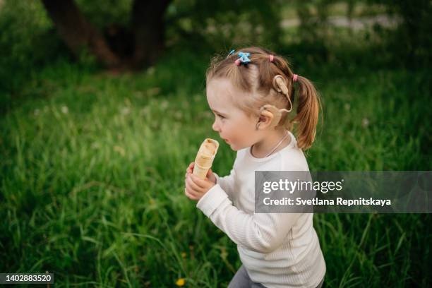 toddler girl with cochlear implants eating ice cream on the lawn in the grass in the park - cochlea implant stock pictures, royalty-free photos & images