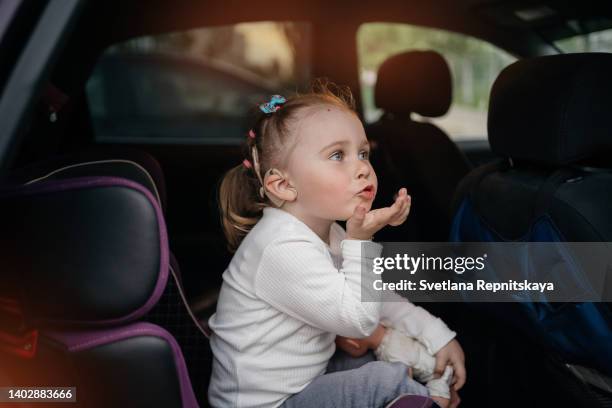 toddler girl with cochlear implants in the car seat sends an air kiss - cochlea implant stock pictures, royalty-free photos & images