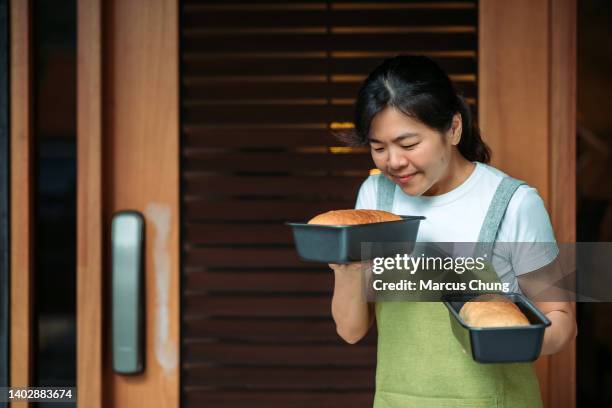asian chinese smiling baker women holding two tray of bread in front yard of house - baker smelling bread stockfoto's en -beelden