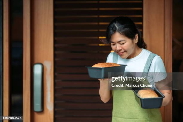 asian chinese smiling baker women holding two tray of bread in front yard of house - baker smelling bread stock pictures, royalty-free photos & images