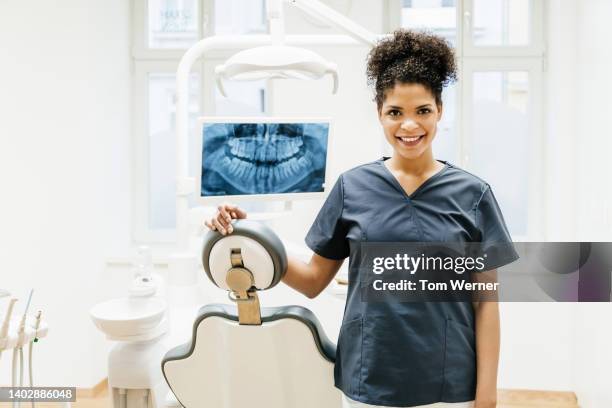 portrait of dental technician standing with hand on dentist chair - dental hygienist stock pictures, royalty-free photos & images