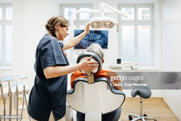 dental technician using overhead lamp to examine patient - sprechstundenhilfe stock-fotos und bilder