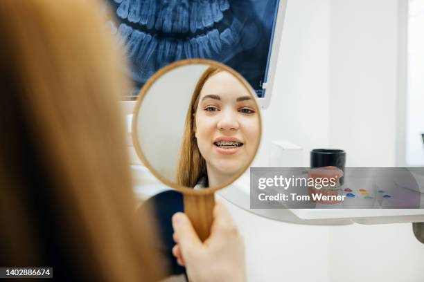reflection of young woman examining newly fitted braces - petite teen girl stock-fotos und bilder