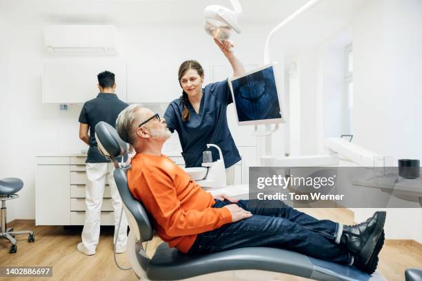 dental assistant adjusting overhead light during check up on patient - tandarts stockfoto's en -beelden