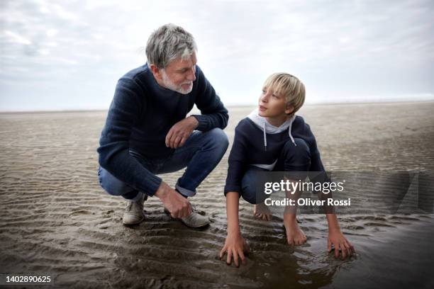 mature man and boy crouching on the beach - grandpa son stock pictures, royalty-free photos & images