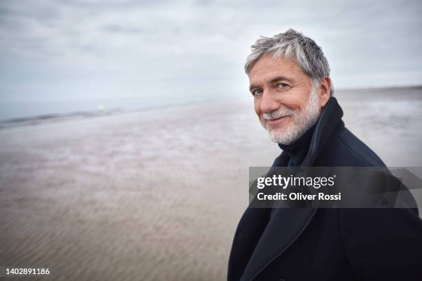 portrait of confident mature man in coat on the beach - overcast portrait stock pictures, royalty-free photos & images