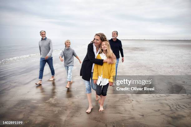 mother hugging daughter with family walking on the beach - barefoot boy fotografías e imágenes de stock