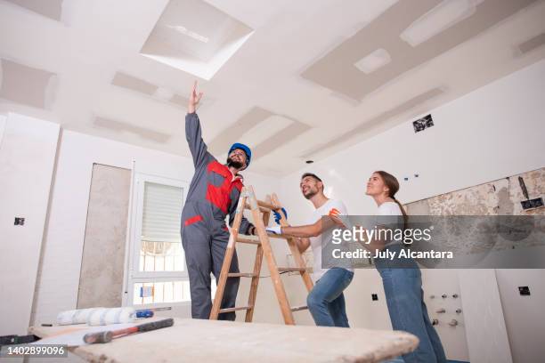 young couple receives advice from an expert bricklayer on the reform of a hatch to access the attic - plasterboard stock pictures, royalty-free photos & images