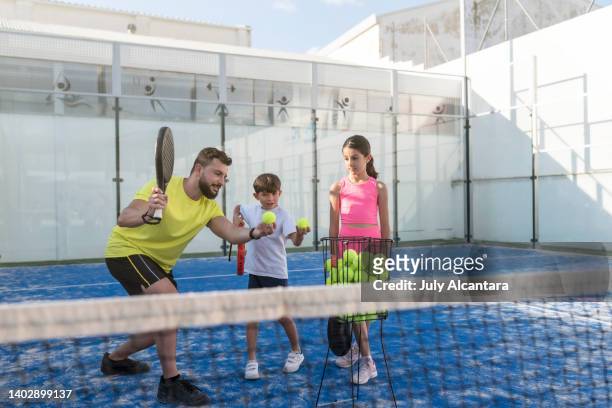 father teaches his children to serve and play paddle tennis on a court - paddle tennis stock pictures, royalty-free photos & images