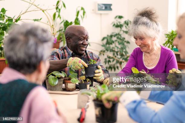 笑顔の年金受給者は鉢植えの植物の世話をすることを楽しんでいます - 老人ホーム ストックフォトと画像
