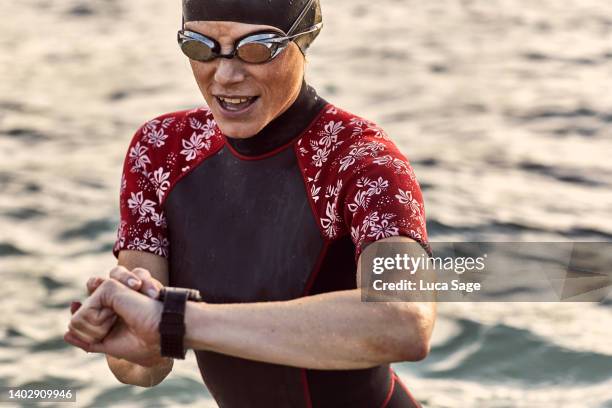 woman in a wetsuit after enjoying a sunset swim in ibiza, checks her smart watch - early termination foto e immagini stock