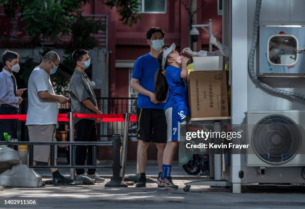Girl stands on her toes as she gets a nucleic acid test after a recent COVID-19 outbreak at a testing site on June 14, 2022 in Beijing, China....