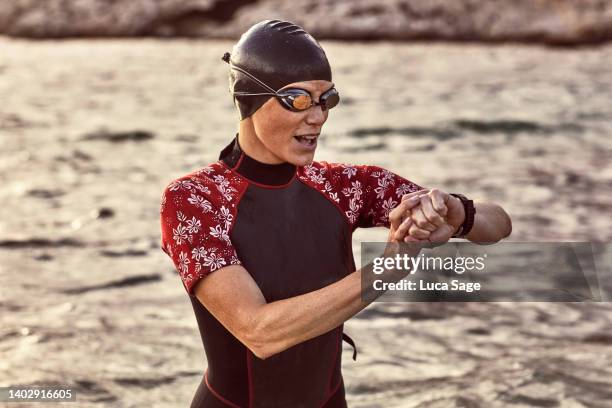 woman in wetsuit sets her smart watch to record before a sunset swim in ibiza - early termination foto e immagini stock