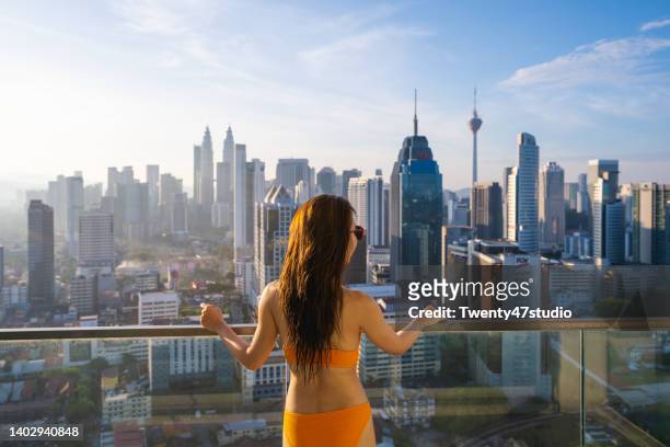 rear view of woman in bikini enjoys city high angle view of kuala lumpur city - luxury hotel room stock pictures, royalty-free photos & images